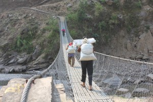 Nepal, Nuwakot: dopo aver ricevuto sacchi di cibo, le persone lo portano al villaggio con un ponte sospeso.