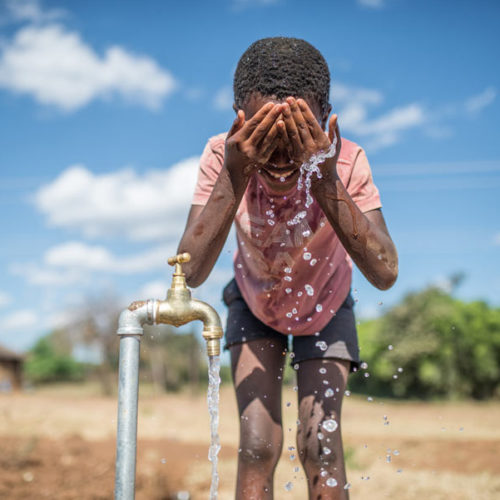 Purity (10 anni) si bagna il viso con l'acqua di un rubinetto collegato a un sistema idrico solare, Zimbabwe