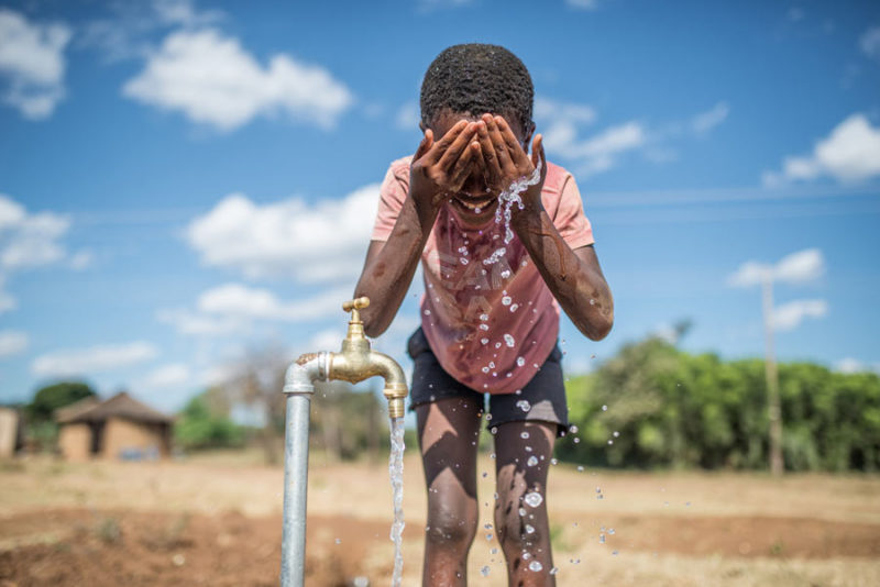 Purity (10 anni) si bagna il viso con l'acqua di un rubinetto collegato a un sistema idrico solare, Zimbabwe