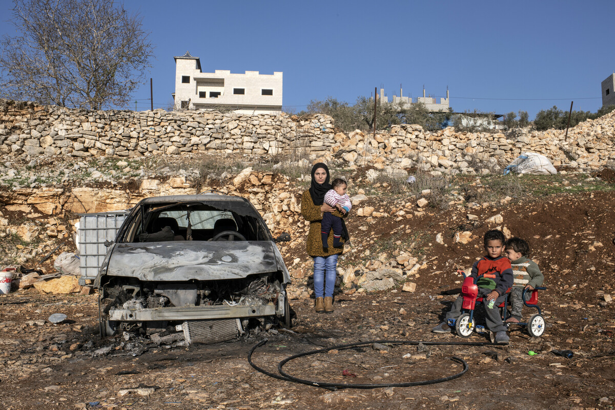 Una madre e la sua famiglia sono vicini a una macchina distrutta a Gaza