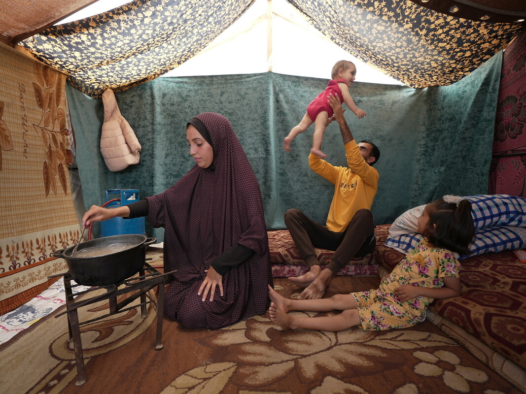 Duaa Abu Sabha cucina nella sua tenda nell'area di Al-Mawasi, nel Governatorato di Khan Yunis, mentre suo marito gioca con i loro bambini Foto: Alef Multimedia/Oxfam