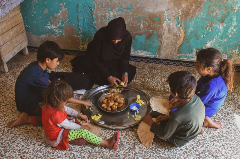 Aisha Ahmad, 35 anni, vedova e capofamiglia di una famiglia di nove persone che vive nelle zone rurali di Aleppo, mostrata con i suoi bambini mentre mangiano patate bollite che di solito mangiano quando non possono permettersele per acquistare altri prodotti alimentari.