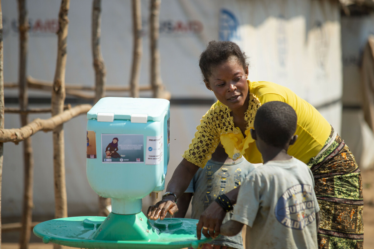 Lumbumba, 41 anni, mostra ai suoi figli piccoli come utilizzare il nuovo lavamani dopo averlo riempito di acqua pulita. Credit: Arlette Bashizi/Oxfam