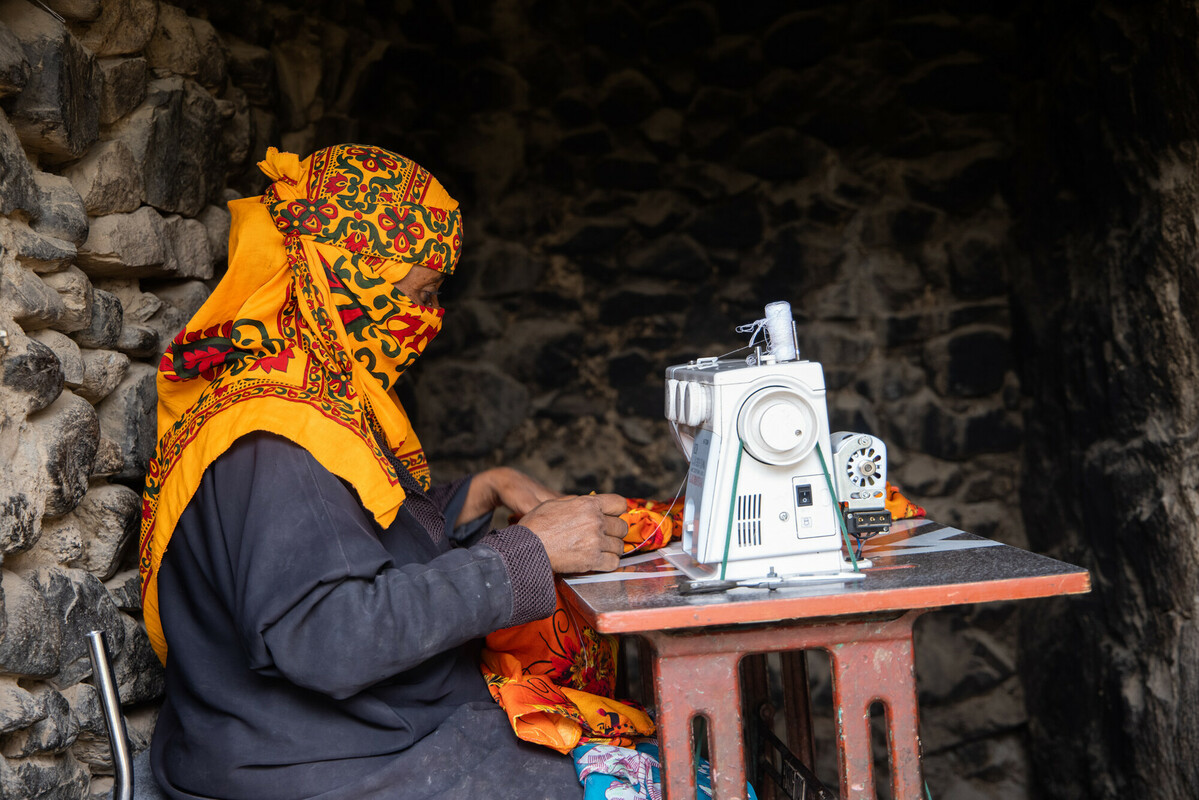 La madre di Munadhel, Mona*, è seduta alla macchina da cucire mentre confeziona vestiti nella loro casa in un piccolo villaggio nel sud dello Yemen. *nome modificato