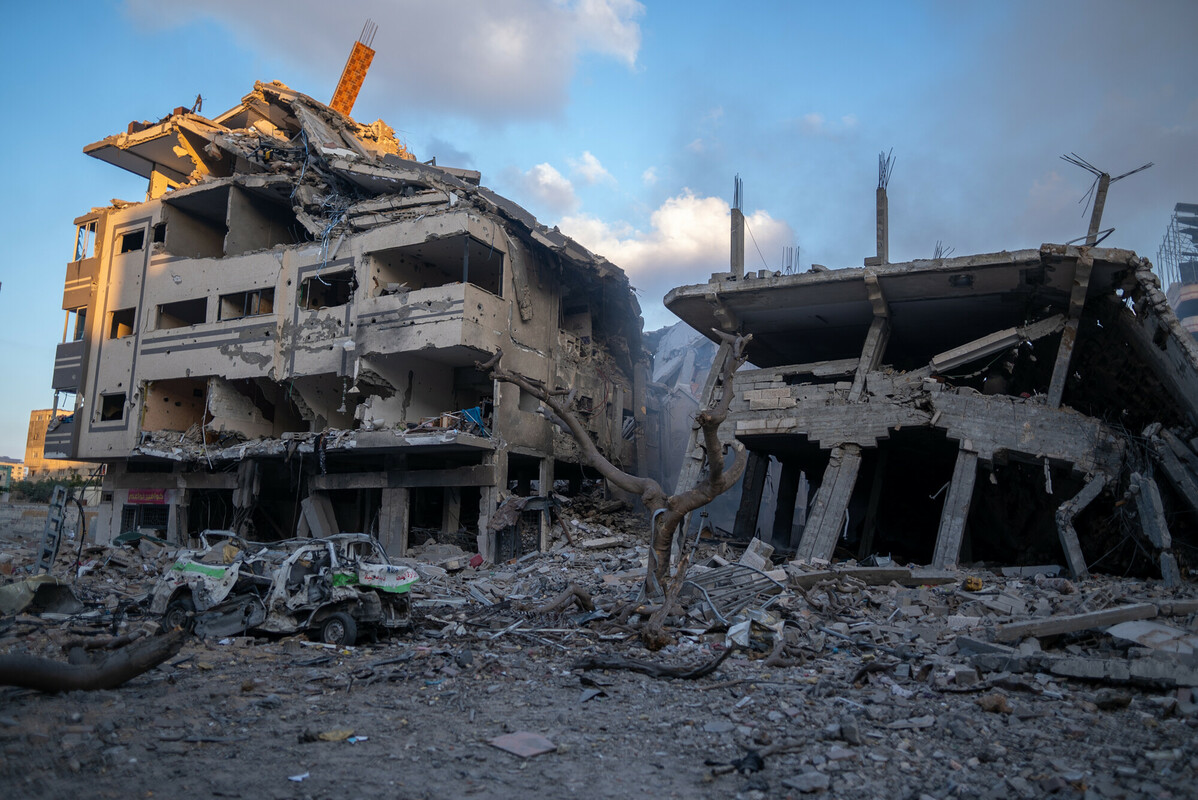 Vista di Gaza con edifici distrutti e sfollati palestinesi in fuga, simbolo della crisi umanitaria e della sofferenza della popolazione civile.