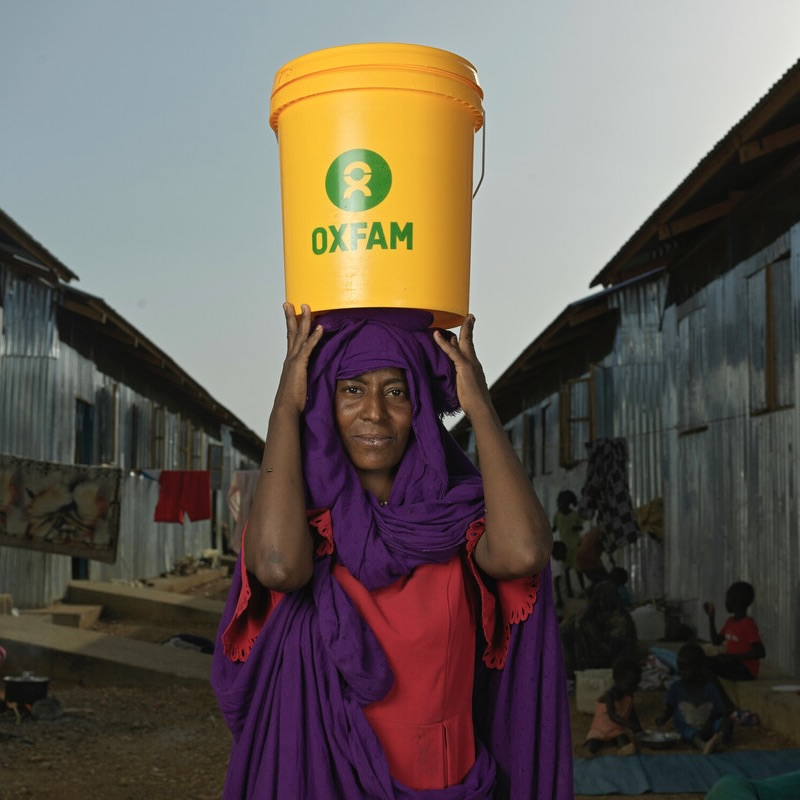 Zinab Alzaki Mohammed Alnur, 20 anni, rifugiato sudanese sfollato a causa della guerra, trasporta un secchio d'acqua nel centro di transito di Renk. Oxfam è il principale partner WASH a supporto di migliaia di rifugiati.