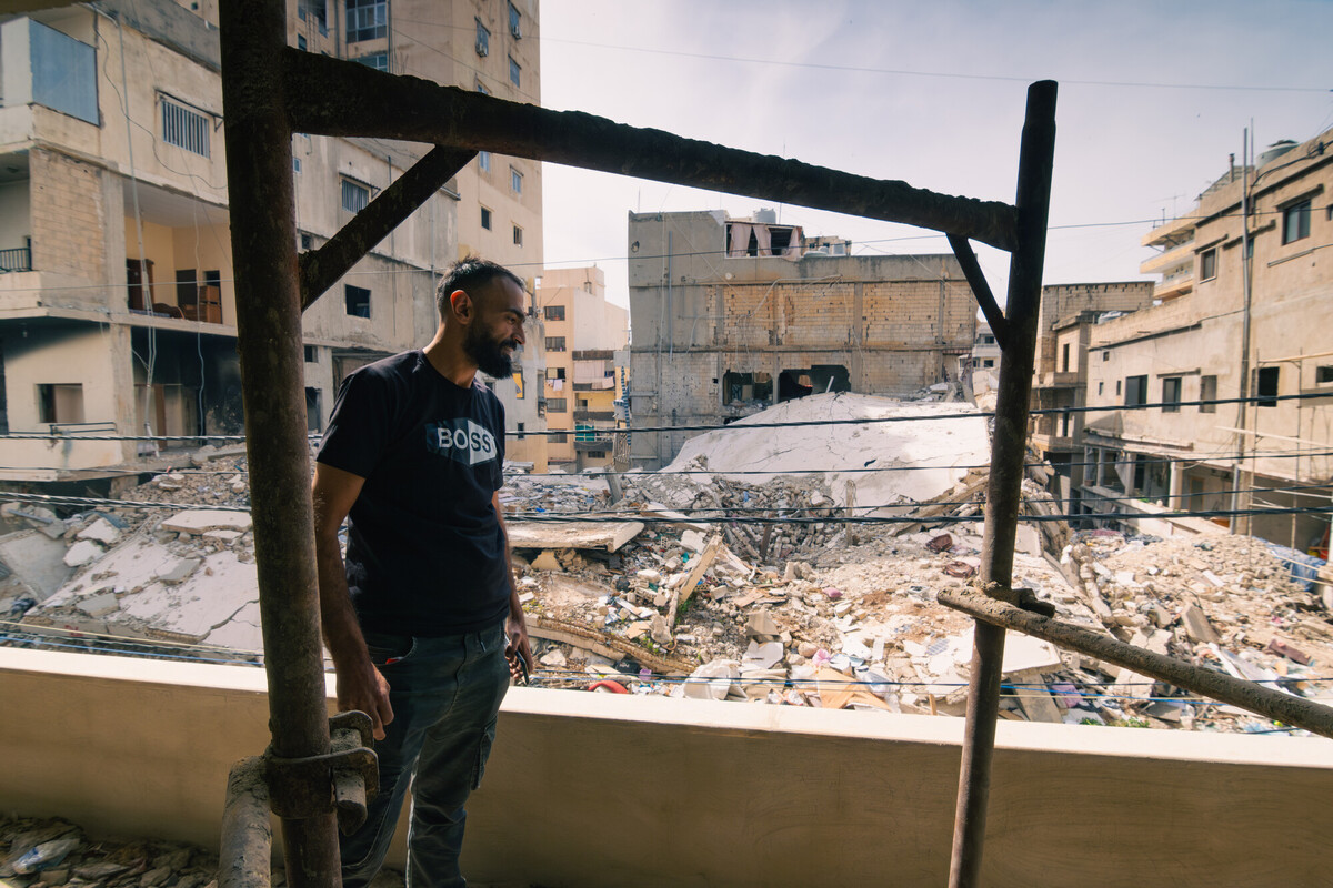 Ali sul balcone di casa sua e osserva la distruzione che si estende nel suo quartiere nel sud del Libano. Dietro di lui, edifici crollati. L'impatto ha causato anche la distruzione della sua casa. Credit: Christian Harb/Oxfam 