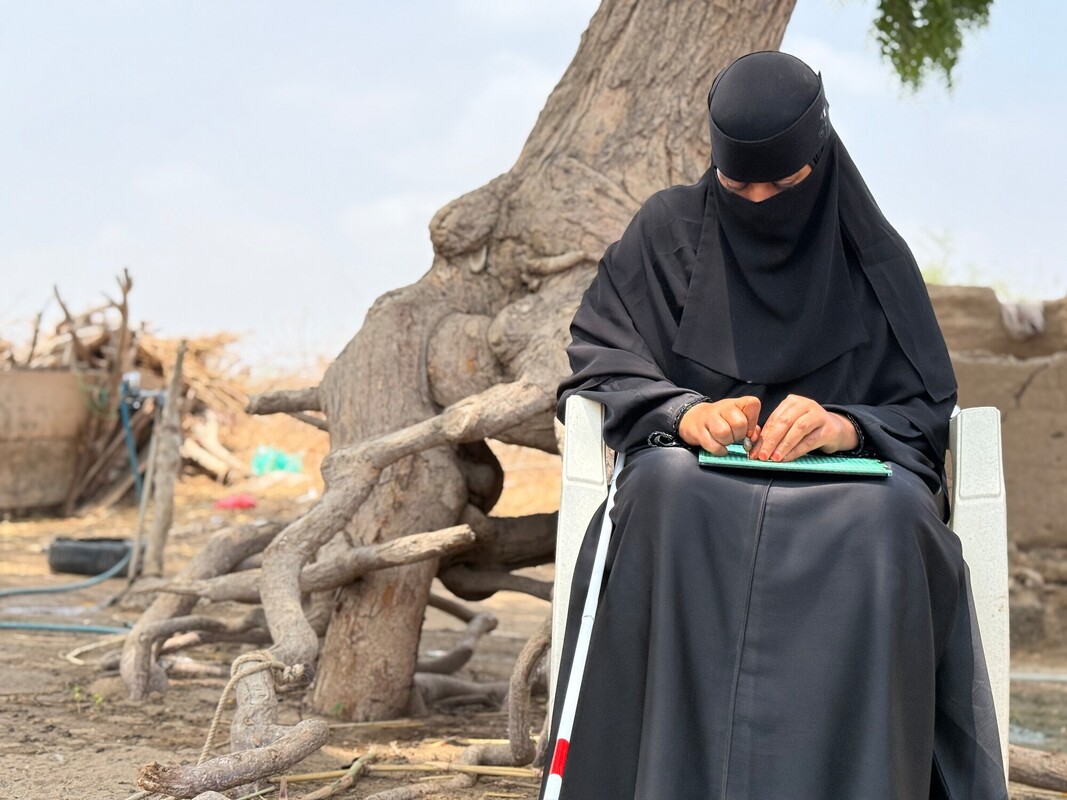 Sanaa legge usando le dita, nel cortile della sua casa a Lahj/Bir Alkadama. Credit: Abdulbari Othaman/Oxfam
