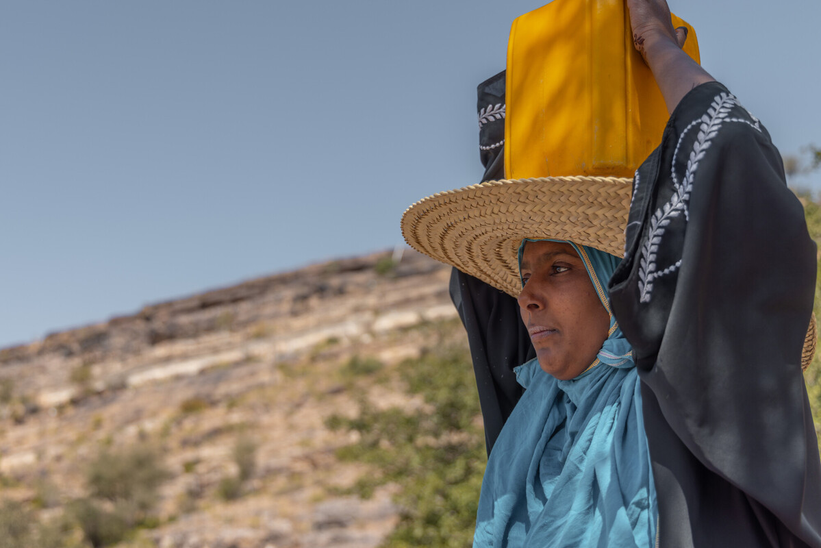 Rawya tiene in equilibrio sulla testa il pesante contenitore, durante il suo lungo viaggio quotidiano per raccogliere l'acqua, un viaggio che richiede ore e le prosciuga le forze.