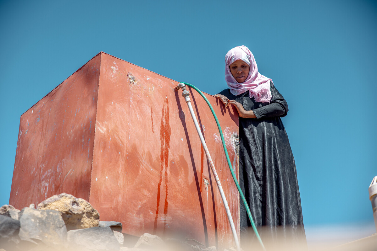 Abeer, in piedi accanto al serbatoio dell’acqua installato vicino la sua casa, che finalmente fornisce acqua pulita alla sua famiglia. Credit: Ahmed Albasha / Oxfam