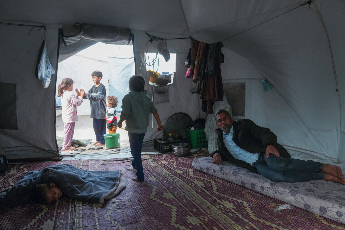 I figli di Bilal, beneficiario delle attività di assistenza in denaro di Oxfam a Gaza, giocano fuori dalla loro tenda in un accampamento di fortuna a Gaza, mentre lui è seduto all’interno della tenda. Credit: Mosab Al-Borno/ Alef Multimedia/ Oxfam